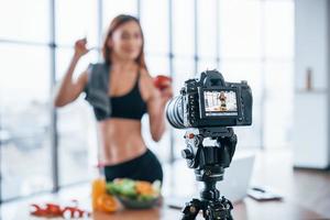 Vloggerin mit sportlichem Körper, die drinnen neben einem Tisch mit gesundem Essen steht foto