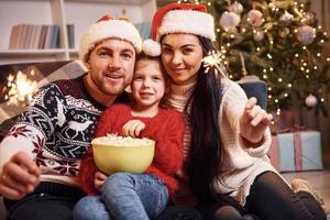 glückliche familie drinnen in weihnachtsmützen haben spaß zusammen und feiern das neue jahr foto