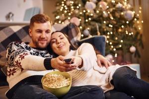 junges Paar umarmt sich drinnen im weihnachtlich dekorierten Raum foto