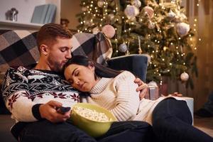 junges paar drinnen in einem weihnachtlich dekorierten zimmer, das auf dem boden sitzt und das neue jahr feiert foto