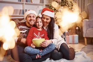 glückliche familie drinnen in weihnachtsmützen haben spaß zusammen und feiern das neue jahr foto