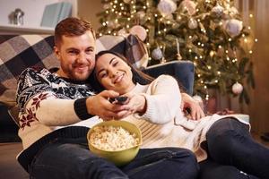 junges Paar umarmt sich drinnen im weihnachtlich dekorierten Raum foto