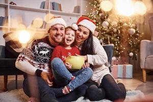 glückliche familie drinnen in weihnachtsmützen haben spaß zusammen und feiern das neue jahr foto