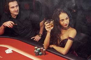 Elegante junge Leute sitzen am Tisch und spielen Poker im Casino foto