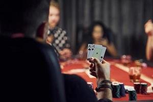 Typ hat ein Paar Asse. Gruppe eleganter junger Leute, die zusammen im Casino Poker spielen foto