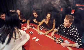 Gruppe eleganter junger Leute, die zusammen im Casino Poker spielen foto