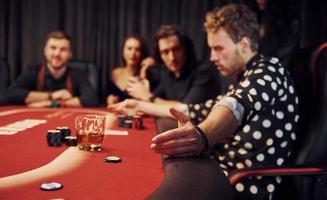 Seitenansicht einer Gruppe eleganter junger Leute, die gemeinsam im Casino Poker spielen foto