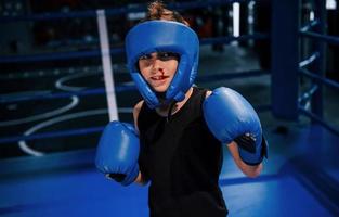 kleiner Junge in Schutzkleidung und mit Nasenblutentraining im Boxring foto