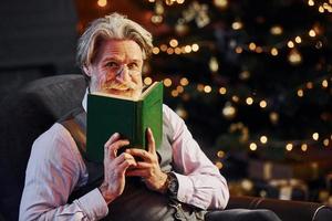 Porträt eines stilvollen Seniors mit grauem Haar und Bart. hält Buch mit Licht kommt davon foto