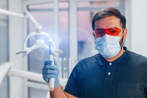 Porträt des Zahnarztes in roter Schutzbrille und mit Werkzeug in der Hand, das drinnen in der Klinik steht foto