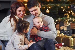 schönes kaukasisches paar, das weihnachten zuhause mit ihrem kleinen sohn und ihrer tochter feiert foto