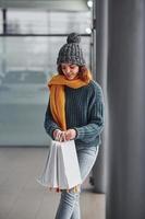 schönes fröhliches mädchen in gelbem schal und in warmer kleidung, die drinnen mit einkaufstüten in den händen steht foto