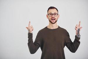 junger Mann mit Sonnenbrille, der drinnen vor weißem Hintergrund steht foto