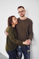 glückliches multiethnisches Paar in Freizeitkleidung ist drinnen im Studio zusammen. Kaukasier mit asiatischer Freundin foto