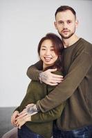 glückliches multiethnisches Paar in Freizeitkleidung, das sich drinnen im Studio umarmt. Kaukasier mit asiatischer Freundin foto