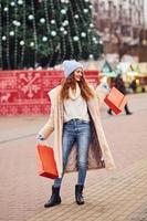 Junges Mädchen in warmer Kleidung mit Einkaufstüten in den Händen macht einen Spaziergang im Freien in der Stadt foto