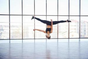 Junge sportliche Frau in Sportbekleidung springt und macht sportliche Tricks gegen Fenster in der Luft foto