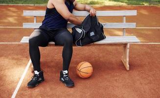 sitzt mit schwarzer Tasche und bereitet sich auf das Spiel vor. afroamerikaner spielt basketball auf dem platz im freien foto