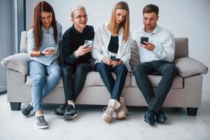 gruppe von freunden, die zusammen auf dem sofa mit telefonen sitzen foto