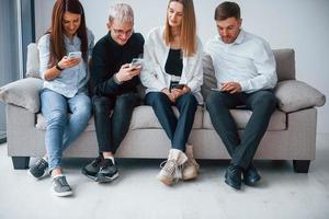 gruppe von freunden, die zusammen auf dem sofa mit telefonen sitzen foto