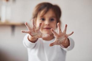 Positives kleines Mädchen, das Hände mit Mehl in der Küche zeigt foto