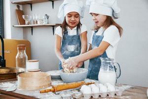 Zwei kleine Mädchen in blauer Kochuniform bereiten Essen in der Küche zu foto