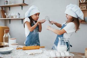 Zwei kleine Mädchen in blauer Kochuniform haben Spaß und bereiten Essen in der Küche zu foto