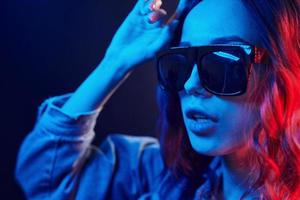 Porträt eines jungen Mädchens mit Sonnenbrille in rotem und blauem Neon im Studio foto