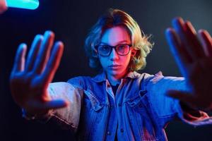 Porträt eines jungen alternativen Mädchens in Brille mit grünen Haaren in rotem und blauem Neonlicht im Studio foto