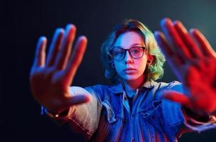 Porträt eines jungen alternativen Mädchens in Brille mit grünen Haaren in rotem und blauem Neonlicht im Studio foto