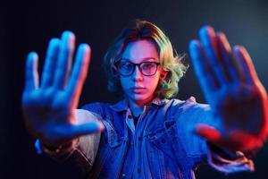 Porträt eines jungen alternativen Mädchens in Brille mit grünen Haaren in rotem und blauem Neonlicht im Studio foto