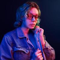 Porträt eines jungen alternativen Mädchens in Brille mit grünen Haaren in rotem und blauem Neonlicht im Studio foto