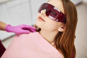 Kleines Mädchen mit Schutzbrille, das den Zahnarzt in der Klinik besucht. Konzeption der Stomatologie foto