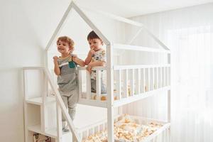 Zwei kleine Jungen ruhen sich aus und haben gemeinsam Spaß drinnen im Schlafzimmer foto