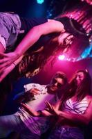 Blick von unten auf junge Leute, die sich im Nachtclub mit bunten Laserlichtern amüsieren foto
