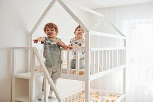 Zwei kleine Jungen ruhen sich aus und haben gemeinsam Spaß drinnen im Schlafzimmer foto