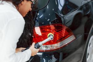 frau mit ausrüstung, die modernes auto reinigt. Konzeption des Dienstes foto