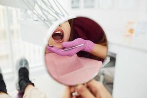 schaut in den Spiegel. kleines mädchen, das zahnarzt in der klinik besucht. Konzeption der Stomatologie foto