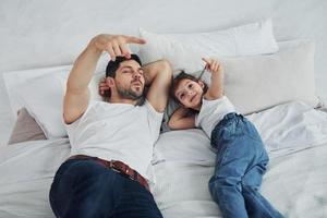 glücklicher vater mit seiner tochter, die zusammen freizeit zu hause verbringt. sich aufs Bett legen foto