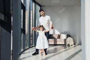 Glücklicher Vater mit seiner Tochter im Kleid, die lernt, wie man zu Hause zusammen tanzt foto