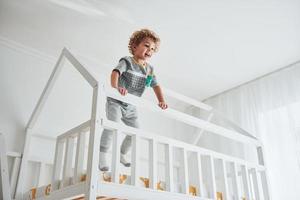 süßer kleiner Junge ruht sich aus und hat Spaß drinnen im Zimmer auf dem Bett foto