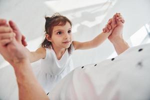 Glücklicher Vater mit seiner Tochter im Kleid, die lernt, wie man zu Hause zusammen tanzt foto