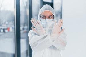 Stoppen Sie das Viruszeichen. Porträt einer Ärztin in Laborkittel, Schutzbrille und Maske