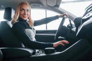 Seitenansicht der schönen Blondine in eleganter Kleidung, die in einem modernen Auto sitzt foto