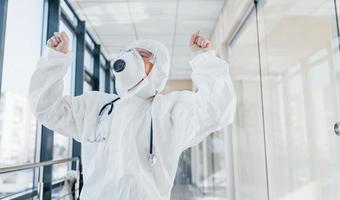 Sieg feiern. Ärztin in Laborkittel, Schutzbrille und Maske im Innenbereich foto