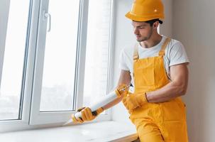 Handwerker in gelber Uniform arbeitet mit Klebstoff für Fenster im Innenbereich. haussanierungskonzept foto