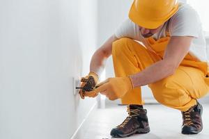 handwerker in gelber uniform arbeitet mit strom und installiert neue steckdose. haussanierungskonzept foto