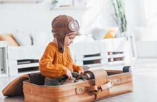 kleine jungen im retro-pilotenkostüm haben spaß und sitzen tagsüber im koffer drinnen foto