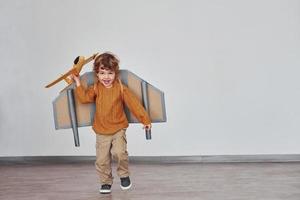 kleiner Junge in Retro-Pilotenuniform, der drinnen mit Spielzeugflugzeug läuft foto