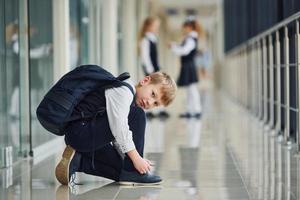 Junge, der auf dem Boden sitzt. Schulkinder in Uniform zusammen im Korridor foto